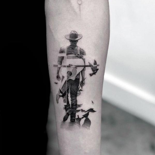 Black and gray tattoo of a cowboy walking away with a guitar, featuring a fragmented design with birds flying from his silhouette.
