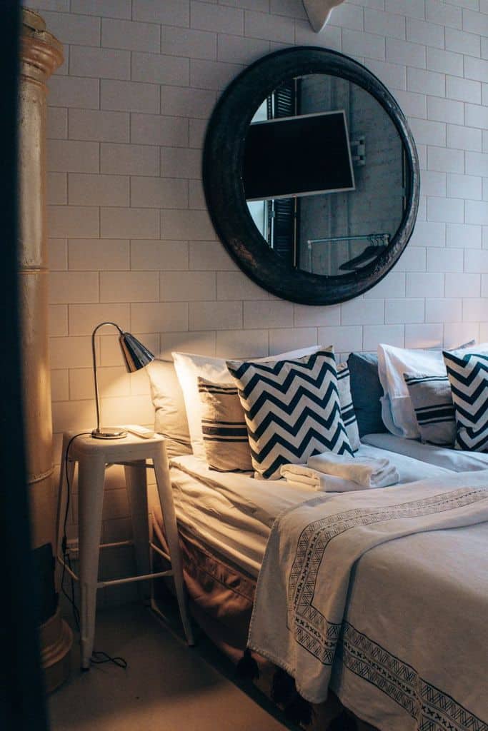 Cozy bedroom with a round mirror, zigzag-patterned pillows, and a bedside lamp on a stool