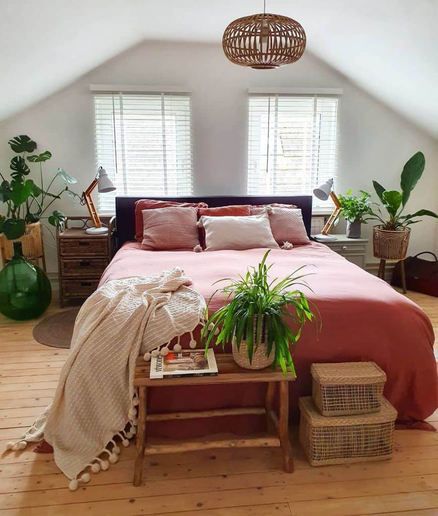 Cozy attic bedroom with pink bedding, potted plants, wicker baskets, and wooden accents.