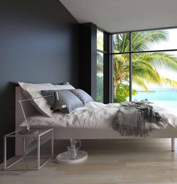 Modern bedroom with a cozy bed, large windows showcasing a tropical beach view, and a sleek bedside table