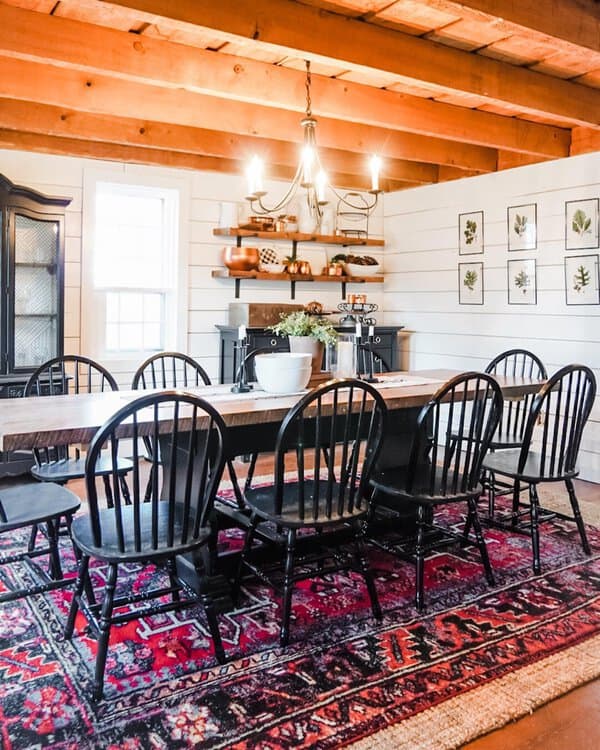 Boho dining room with natural materials, black chairs, exposed wooden beams, and a cozy rug.