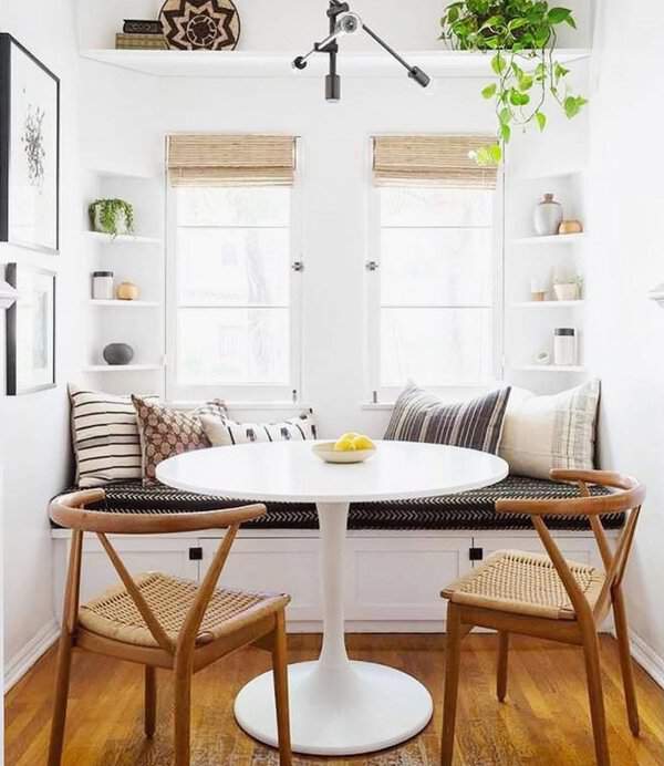 Cozy boho dining nook with a white round table, wishbone chairs, and built-in bench seating.