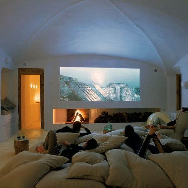 People unwinding on large cushions in a cozy home theater with a fireplace and movie screen