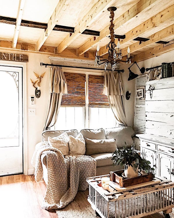 A cozy cottage living room featuring an unfinished wooden ceiling, comfortable furniture, and a rustic vibe with natural light streaming in through the windows