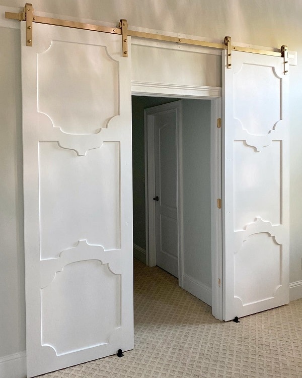 Elegant white sliding barn doors with decorative panel design leading to a hallway.