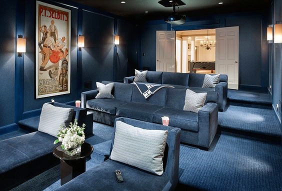 Home theater with blue seating, a projector, and wall art, featuring a cozy ambiance with dim lighting and popcorn on the table