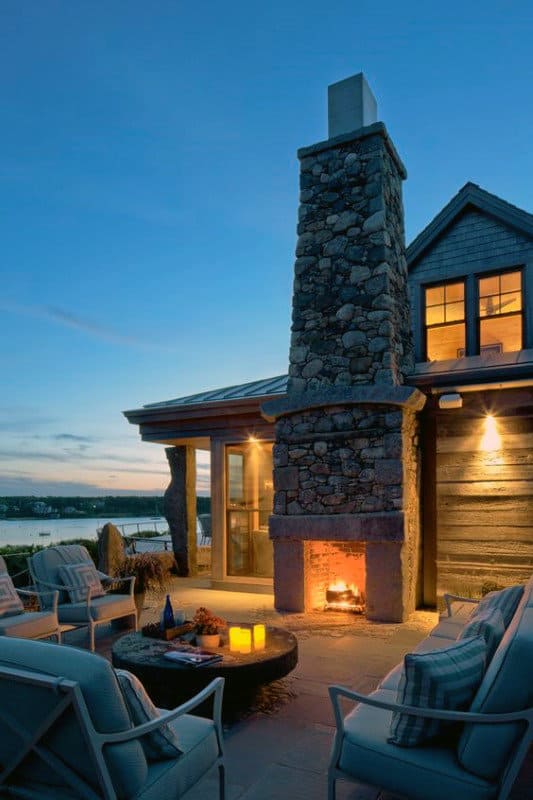 Cozy outdoor patio with stone fireplace, seating area, and ocean view at dusk