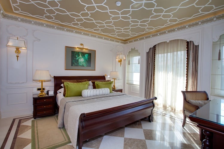 A cozy bedroom featuring a beautifully painted ceiling with intricate patterns, elegant furniture, and large windows that provide natural light, creating a refined and inviting atmosphere