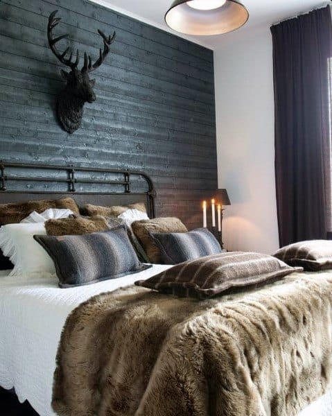 Rustic bedroom with moose head wall art, black paneling, and fur bedding.