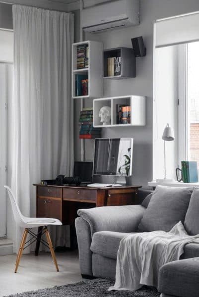A cozy home office with a wooden desk, books, a computer, a gray sofa, and a white chair