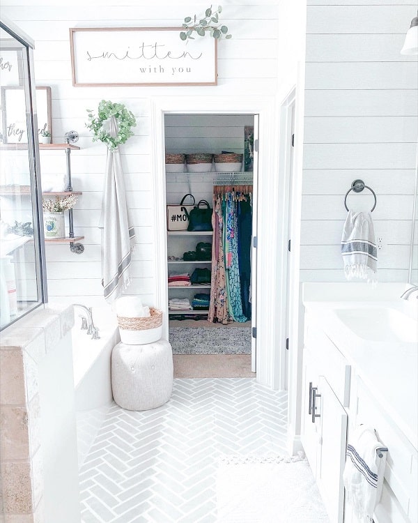 Farmhouse-inspired bathroom with white walls, a bathtub, towels, and a walk-in closet filled with clothes