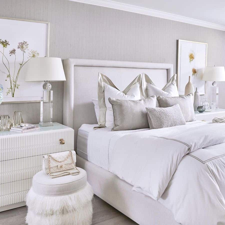 Elegant bedroom with white and beige accents, featuring a plush bed, side tables, and white floral wall art