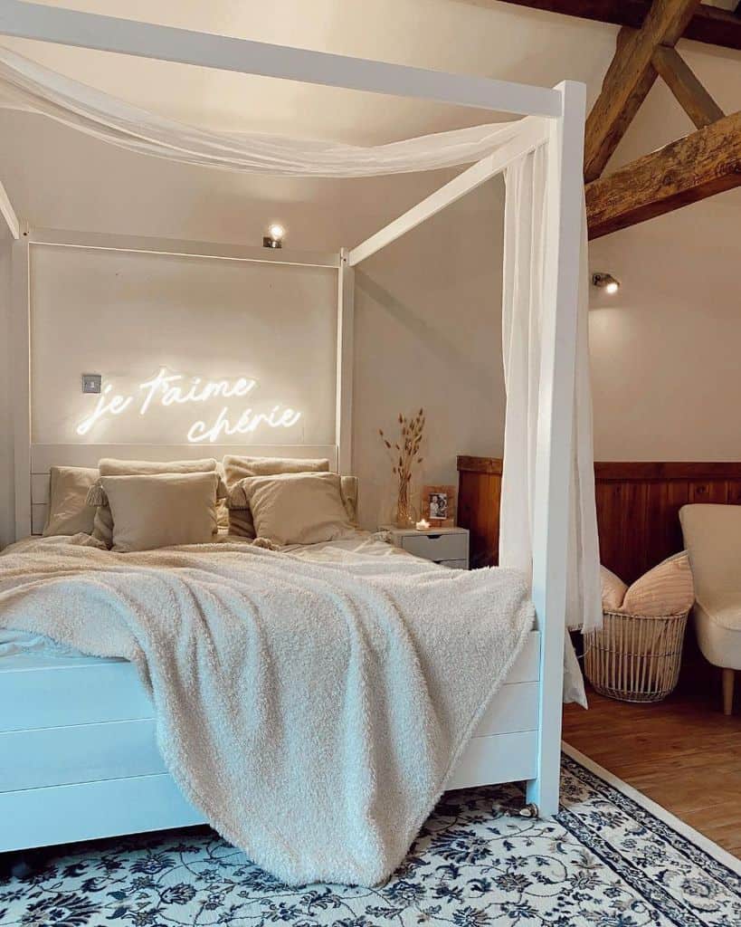 Cozy bedroom with a white canopy bed, beige bedding, and neon sign "je t'aime chérie" on the wall