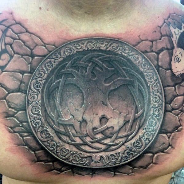 Tattoo of a circular dragon emblem with intricate patterns on a chest, surrounded by cracked stone-like effects