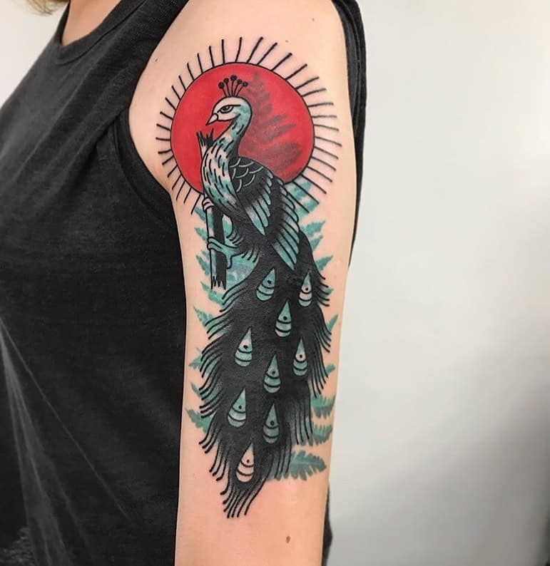 Peacock tattoo with a bold black and red sunburst background, detailed feathers flowing down the arm.