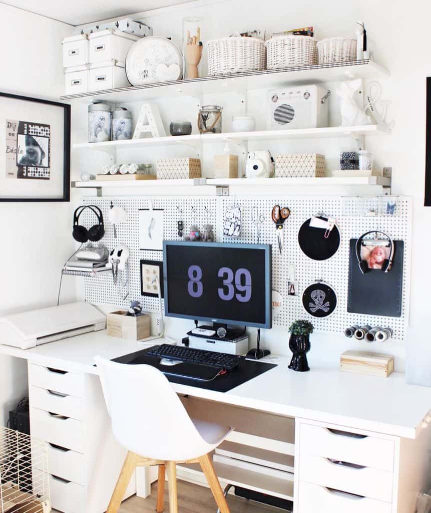 Modern workspace featuring a sleek white desk, pegboard organization, and decorative shelves for craft supplies and personal touches