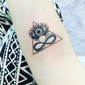 Tattoo of an all-seeing eye atop a triangle with an infinity symbol inside, inked in fine black lines on the forearm.