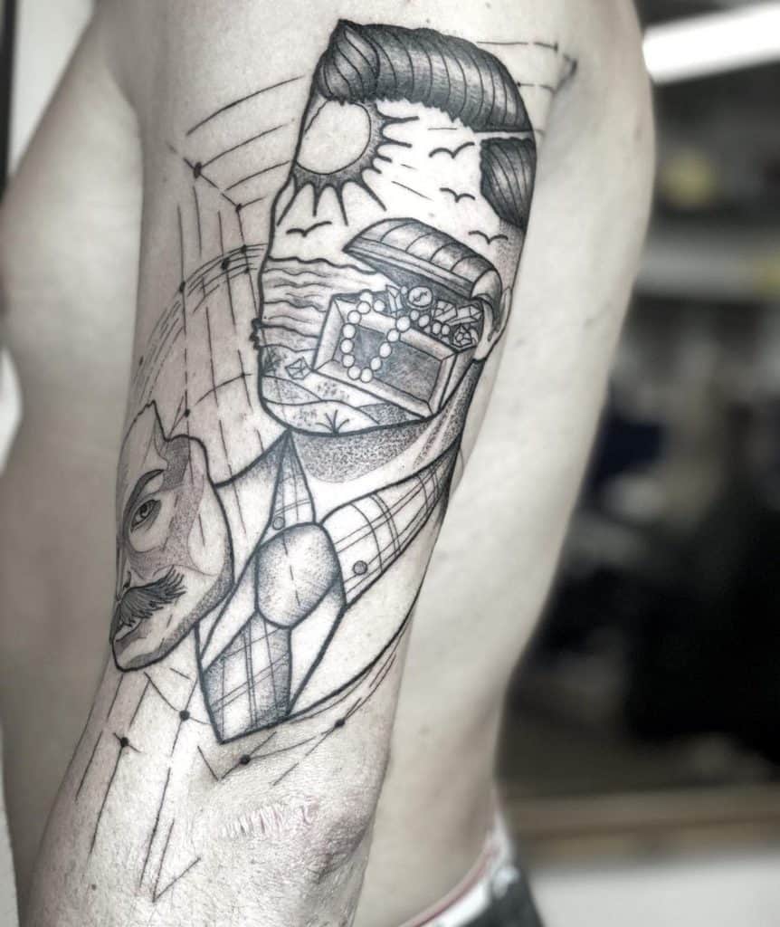 Surrealist arm tattoo of a suited man with a beach scene and treasure chest in place of his face, blending realism with abstract elements.