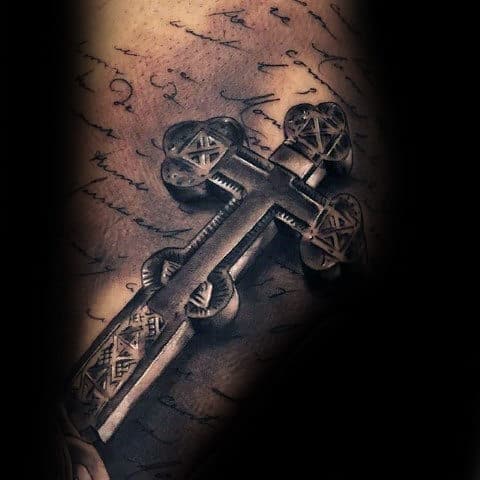 3D tattoo of an intricate cross on a background resembling handwritten script