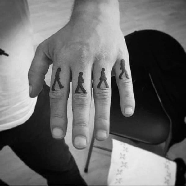 Minimalist Abbey Road silhouette tattoos of The Beatles, each member inked on a different finger to recreate the iconic walking sequence.