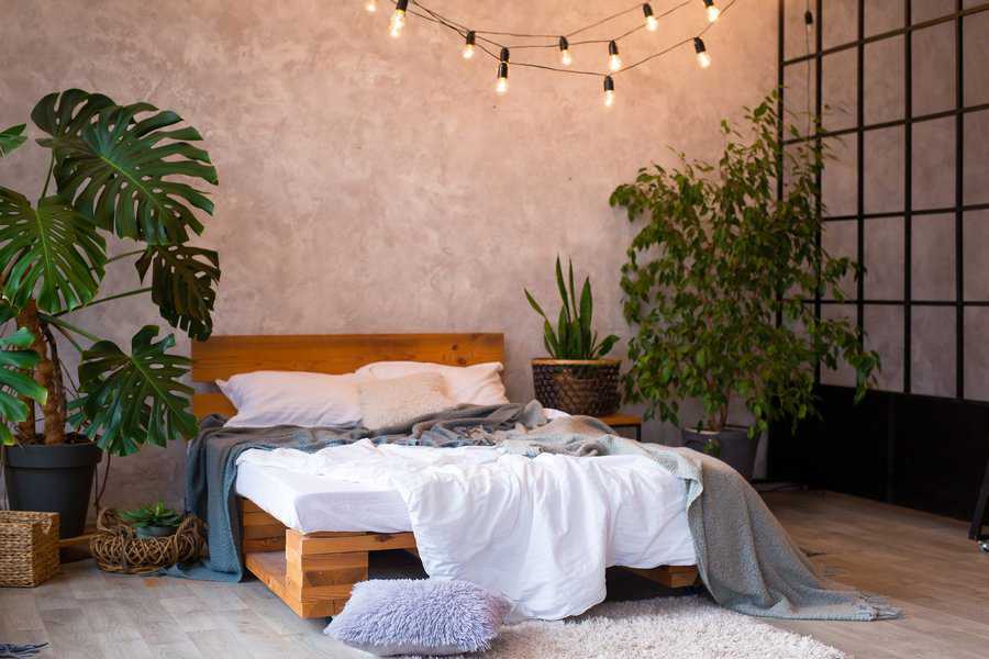 Boho bedroom with pallet bed, string lights, potted plants, and textured gray walls.