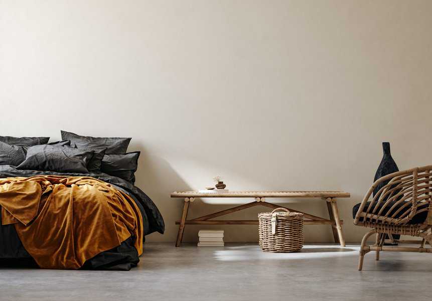 Minimalist bedroom with black and mustard bedding, wicker furniture, and natural decor accents.