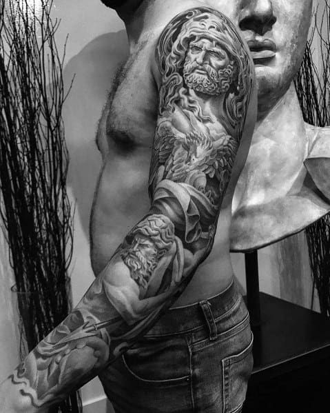 Black and grey full-sleeve tattoo featuring highly detailed Greek mythology-inspired statues with intricate shading and dramatic depth for a powerful design.