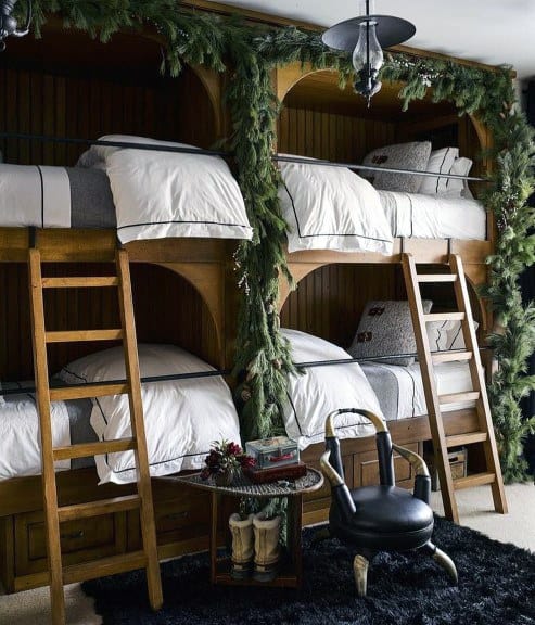 Cozy bunk beds with wooden ladders, adorned with greenery, sit beside a small table and black chair on a plush rug