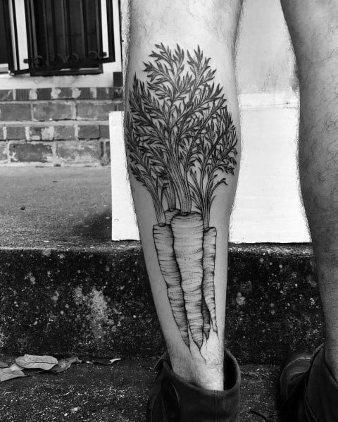 Large black and gray carrot tattoo on the calf, featuring intricate shading and detailed leafy tops for a bold and realistic botanical design.