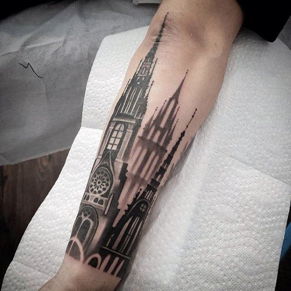 Forearm tattoo of a gothic cathedral with tall spires and stained glass windows, fading into smoky shadows for a surreal effect.