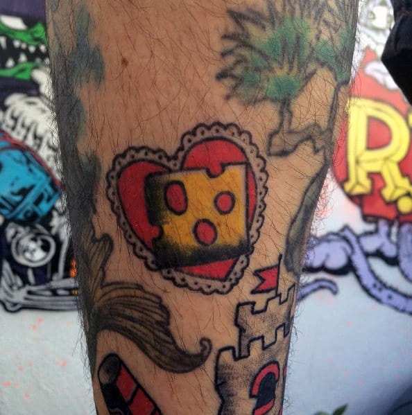 Colorful tattoo of a wedge of cheese inside a red heart with a decorative lace border, featuring bold outlines and traditional-style shading.
