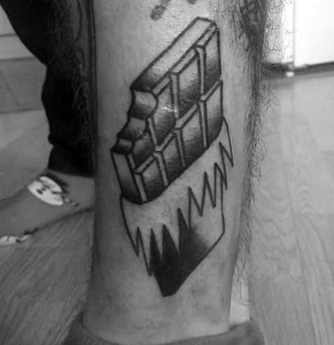 Black and gray tattoo of a bitten chocolate bar in a jagged wrapper, featuring bold shading and a 3D effect for a striking look.