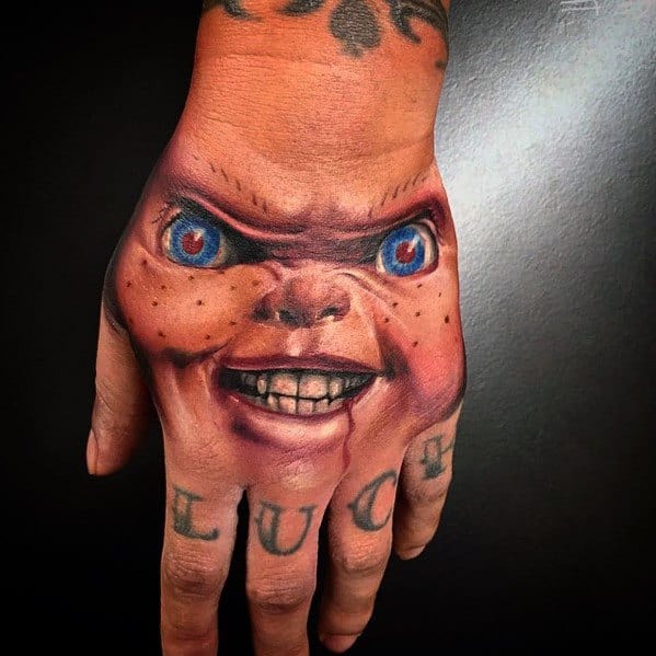 Realistic Chucky hand tattoo with piercing blue eyes, sinister grin, and detailed shading, creating a striking and eerie horror effect.