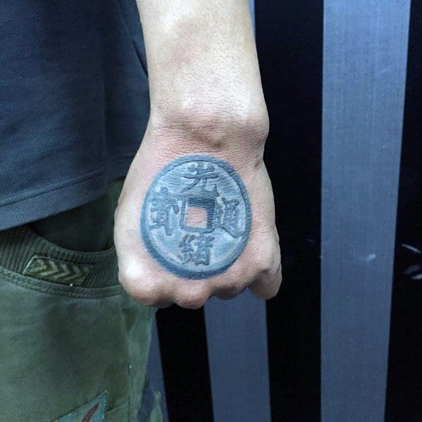 Realistic tattoo of an ancient Chinese coin with a square hole, placed on the hand, symbolizing prosperity and good fortune.