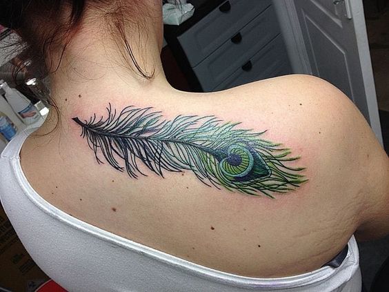 Colorful peacock feather tattoo on the upper back, featuring detailed green and blue hues with intricate shading and fine linework.
