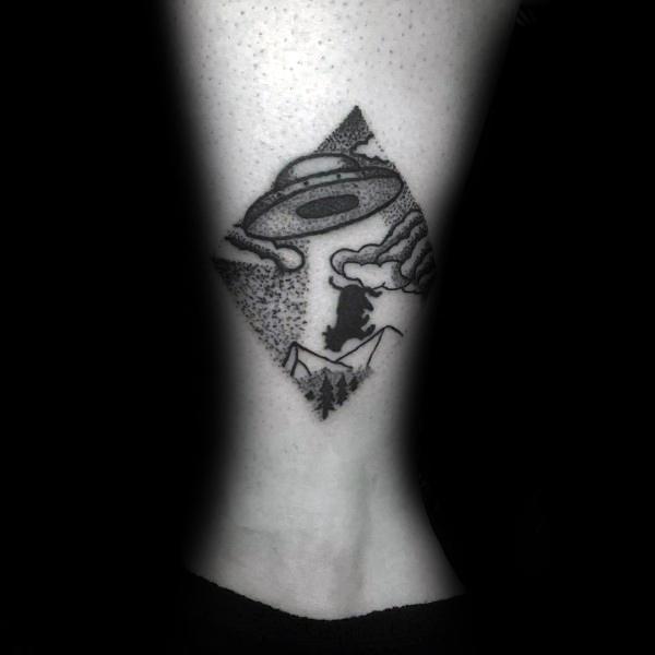 Blackwork UFO abduction tattoo with a cow being lifted over mountains and trees, framed in a diamond shape with dotwork clouds.