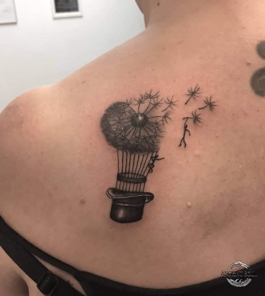 Whimsical dandelion tattoo on the shoulder, blending a hot air balloon and a top hat, symbolizing imagination, freedom, and adventure.