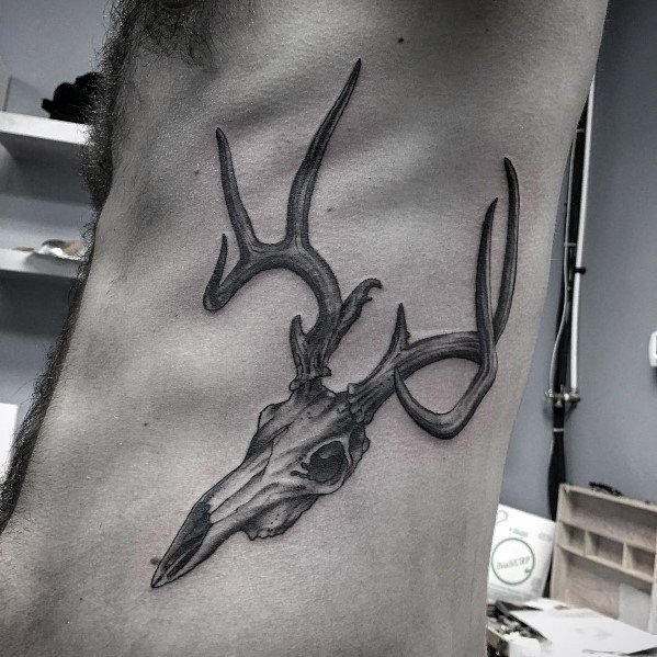 Realistic black and grey elk skull tattoo on the ribcage, featuring intricate shading and fine details for a bold and rugged look.