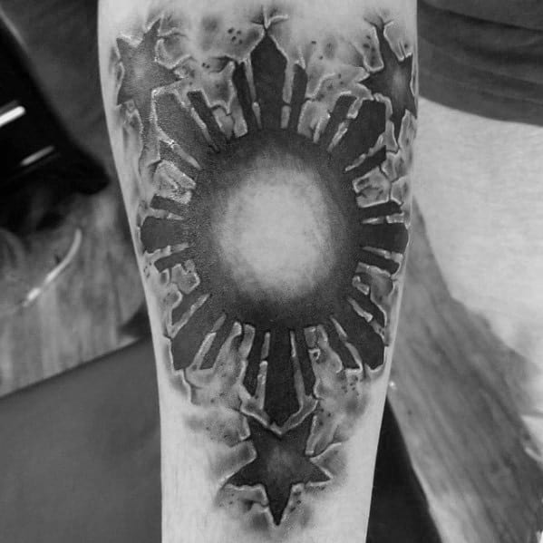 Filipino sun tattoo with a smoky, textured design on the forearm, featuring bold rays and a star below the sun’s glowing center.