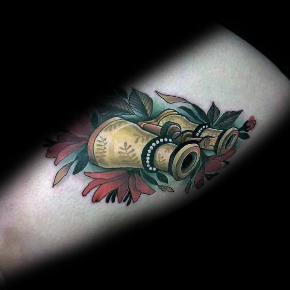 Vintage-style binoculars tattoo with floral elements, featuring warm tones and intricate shading for a classic and artistic look.