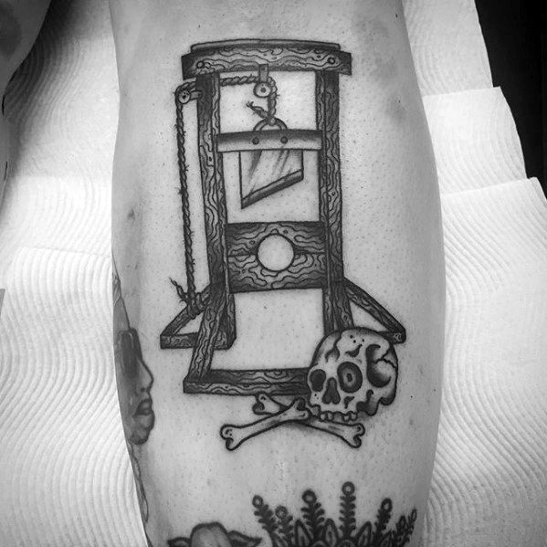 Black and grey guillotine tattoo with rope detailing, a skull and crossbones at the base, and a shaded blade above the hole.
