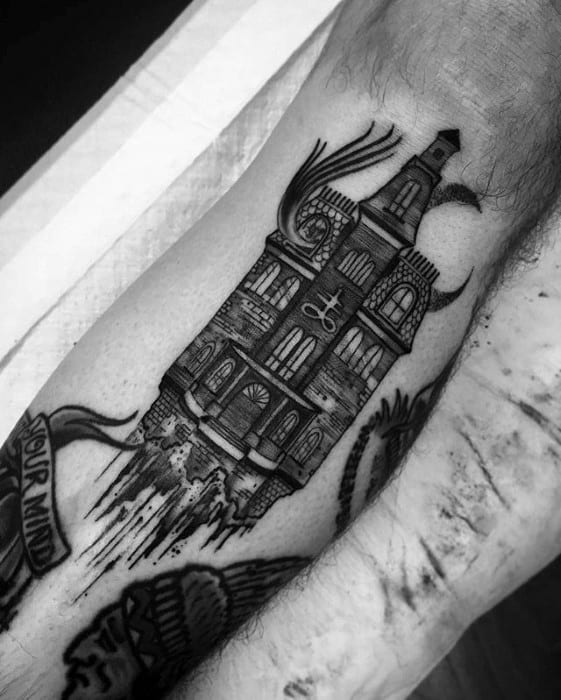 Forearm tattoo of an upside-down haunted house with bats, crescent moon, and “84” on the door, giving a surreal gothic vibe.