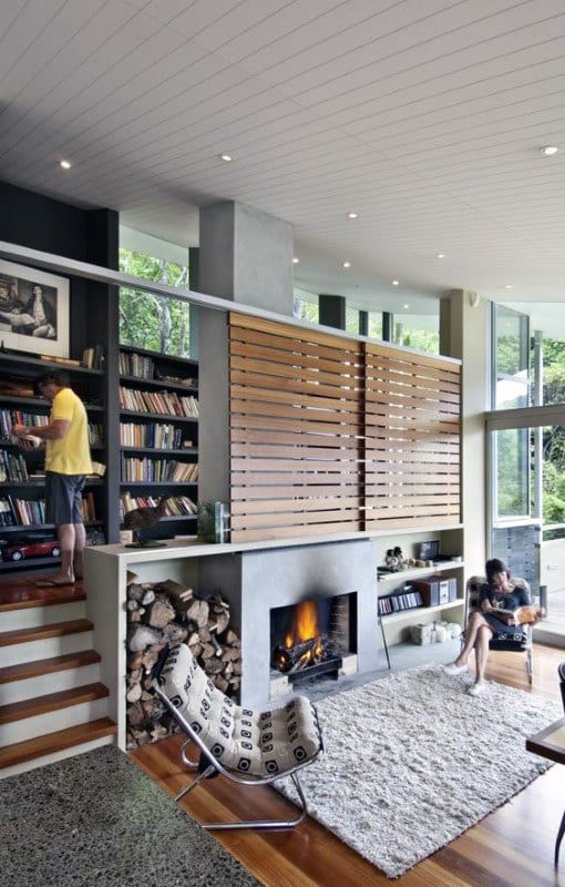 Modern living room with a cozy fireplace, library shelves, large windows, and two people relaxing