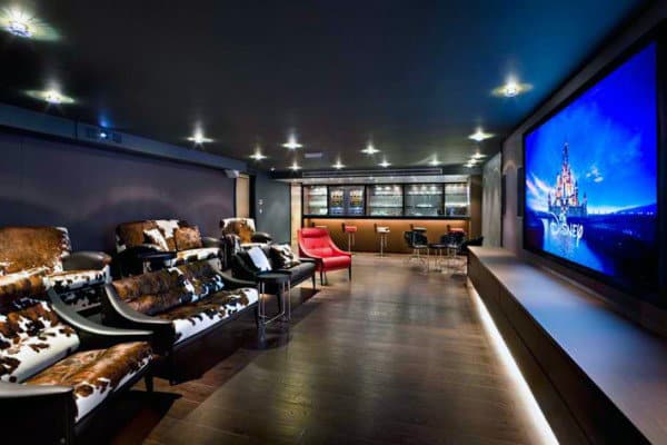Luxurious home theater with cowhide seats, a large screen, a red chair, and a sleek bar area in the back