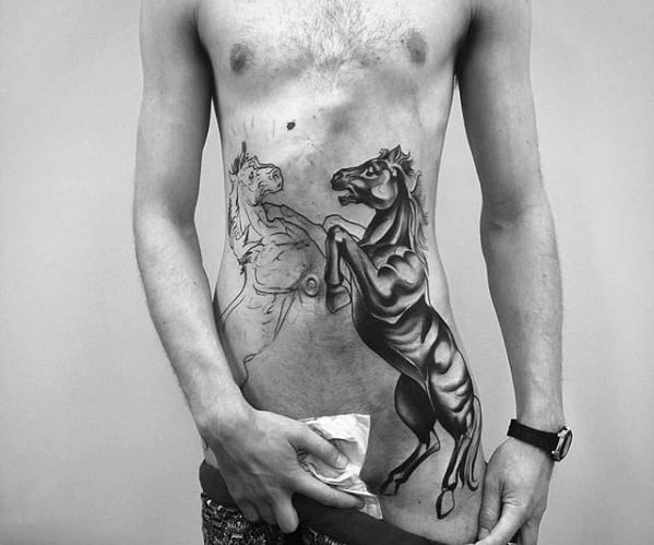 Side torso tattoo of two rearing horses, one fully shaded in black and grey, the other outlined, positioned as if facing each other