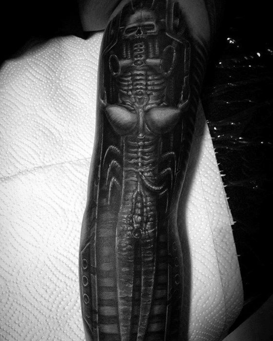Biomechanical tattoo inspired by HR Giger, depicting an alien figure with skeletal and mechanical features along the forearm.