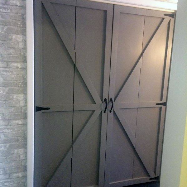 Gray barn-style closet doors with black handles set against a brick wall
