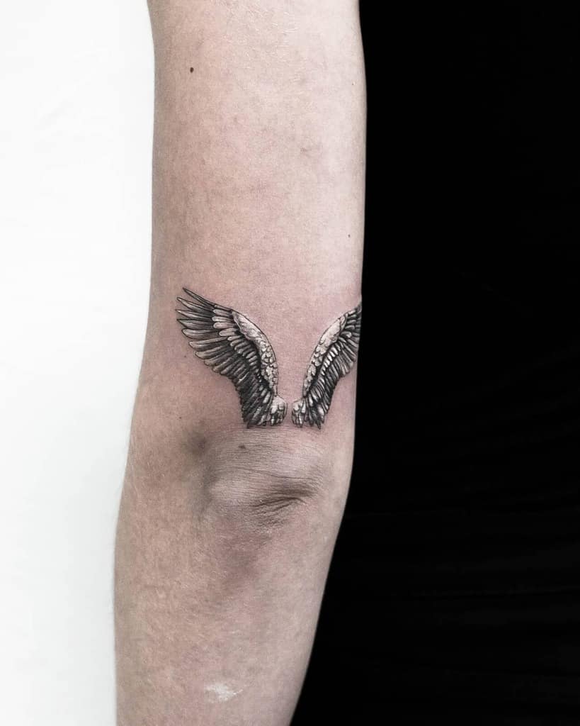 Minimalistic tattoo of angel wings, with fine detailing and shading, creating an elegant and subtle design