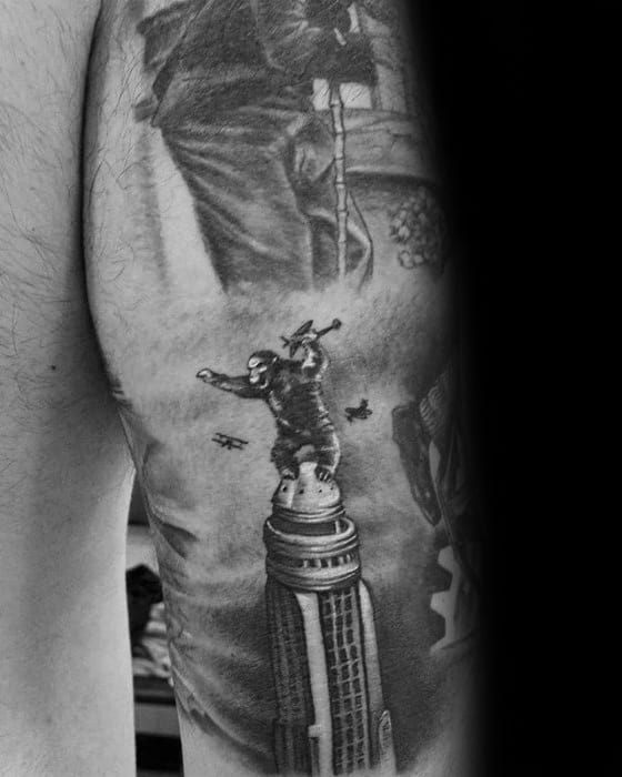 Black and grey tattoo of King Kong on the Empire State Building, swatting at planes in a classic movie scene on upper arm.