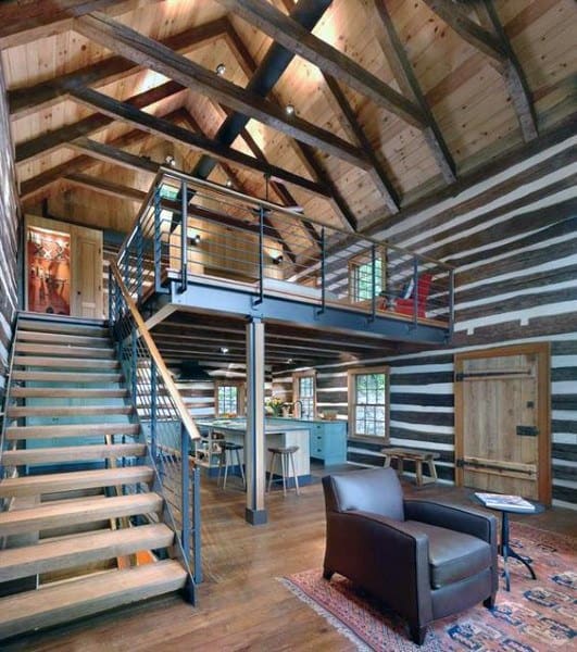 Rustic loft with exposed wood beams, striped log walls, and mezzanine overlooking open living space.